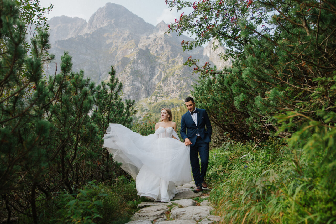 La novia muestra la belleza de su vestido de novia. La pareja se acerca a la cámara, pero sin mirar directamente al encuadre. Se sienten libres y se dan la mano.